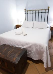 Un dormitorio con una cama blanca con un baúl de madera. en Paraje del Hueznar, en Cazalla de la Sierra