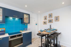 a kitchen with blue cabinets and a table with stools at Smugglers Snug by the sea in Rottingdean