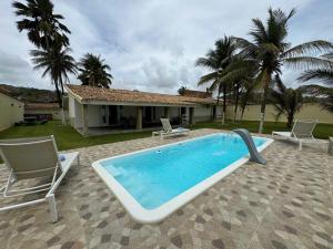 a swimming pool with two chairs and a house at Villa Riacho Doce in Maceió