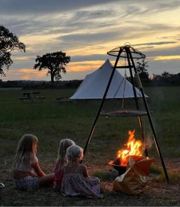 Trzy dziewczyny siedzące przy ogniu przed namiotem w obiekcie Hawthorne Field - Shoreline Escapes w mieście Bransgore
