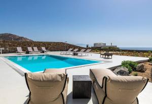 a swimming pool with chairs and a table at Villa Elia Breeze Mykonos in Mikonos