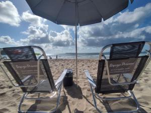 two chairs on a beach under an umbrella at Refúgio Praiano em Bombinhas - Aluguel Temporada in Bombinhas