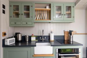una cocina con armarios verdes y fregadero en Deer Lodge Shepherds Hut, en Rowlands Castle
