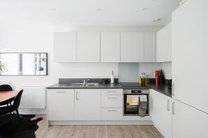 a kitchen with white cabinets and a sink and a table at Beautiful & Contemporary Hackney Retreat in London