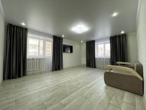 an empty living room with a couch and two windows at 2-комнатная квартира в центре города, Интернациональная 94 in Petropavlovsk