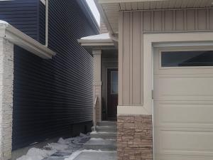 a house with a garage door and snow on the sidewalk at Cozy Basement Suite - private entrance - Free Netflix in Edmonton