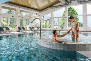 une femme secouant la main d'un homme dans une piscine dans l'établissement Alpenresort Belvedere Wellness & Beauty, à Molveno