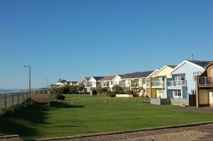 a row of houses on a lawn next to the ocean at Ty Traeth Beach House in Tywyn