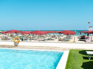 einen Pool neben einem Strand mit Stühlen und Sonnenschirmen in der Unterkunft Hotel Classic in Lido di Savio