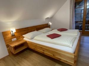 ein Schlafzimmer mit einem Holzbett mit zwei roten Kissen in der Unterkunft Gasthof Thurnerhof in Feld am See