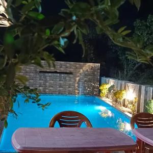 a table and chairs next to a swimming pool at night at ARNAV VILLA Farmhouse & Resort in Vajapūr