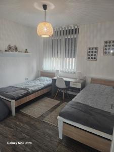 a bedroom with two beds and a desk and a chandelier at Apartman Una in Zrenjanin