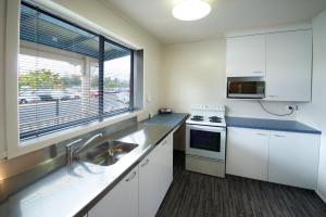 a kitchen with white cabinets and a sink and a window at Ambassador Thermal Motel in Rotorua