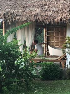 un hombre sentado en una mesa frente a una cabaña en Les Hibiscus Nosy-Be, en Djamandjary