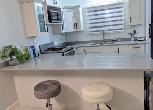 a kitchen with white cabinets and a counter with two stools at Elegant Oasis by the Sea in Saint Annʼs Bay