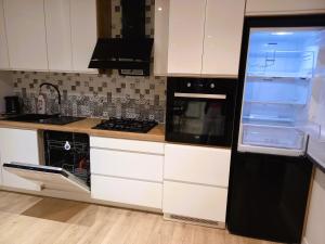 a kitchen with white cabinets and a black refrigerator at Całoroczny dom w sercu Mazur in Węgorzewo