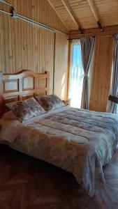 Cama grande en habitación de madera con ventana en Casa Bosque Pichilemu en Rinconada El Sauce