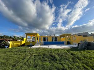 a yellow house in a field with a cloudy sky at Sunset Room With Folding Wall Access To Pool in Aguada