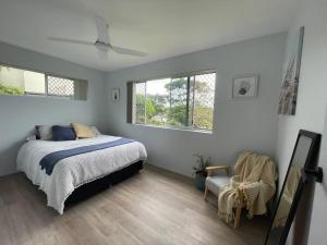 a bedroom with a bed and a chair and two windows at Mindy's by the beach in East Ballina