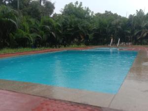 a large blue pool with trees in the background at Sunshine Beach House in Navalur