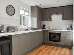 a kitchen with gray cabinets and a clock on the wall at Heather Cottage in Bishop Auckland
