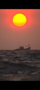 un bateau dans l'océan avec un coucher de soleil dans l'établissement JRN BEACH STAY RESORT-Honnavar, à Honāvar