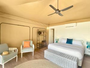 a bedroom with a bed and two chairs and a ceiling fan at Magnetic Glamping Tent 3 in Nelly Bay