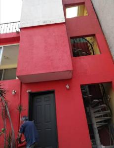 un hombre parado frente a un edificio rojo en Suite equipada 2 camas mat, sala y cocina junto a Tec Santa Fe, en Ciudad de México