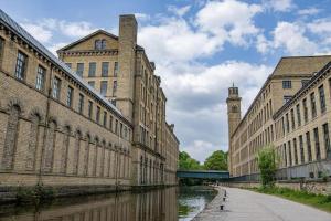 a row of buildings next to a river with a clock tower at Beautiful, Relaxing Home in Central Saltaire in Saltaire