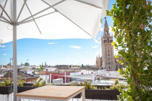 una mesa y una sombrilla en el balcón con una torre del reloj en Hotel Convento La Gloria en Sevilla