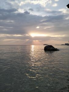 a sunset over the ocean with a rock in the water at Paradise Seaview Homestay in Port Dickson