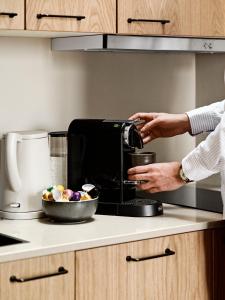 eine Person benutzt eine Kaffeemaschine in einer Küche in der Unterkunft Aura Apartment Hotel in Arhus