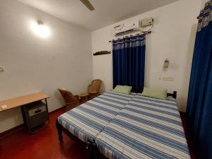 1 dormitorio con cama, escritorio y cortinas azules en Marari Beach Homestay, en Mararikulam