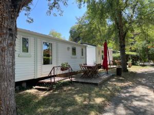 a small white caravan with a table and a tree at CAMPING VERT LAVANDE in Belmont-sur-Rance