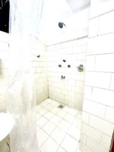 y baño con ducha de azulejos blancos y cortina de ducha. en Luxurious 1BHK with a Pool AniRah Homes in Colva, en Colva
