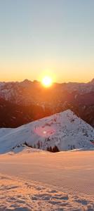 a sunset on a snow covered mountain with the sun setting at Sonnleitn AlpinWell Appartment (Ski in&out + Wellness) in Hermagor