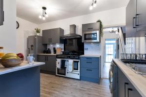 a large kitchen with blue cabinets and appliances at Birmingham Gem-Stylish 5 Bed house near NEC, BHX, HS2 - Huge Parking & Fast WiFi! in Kingshurst
