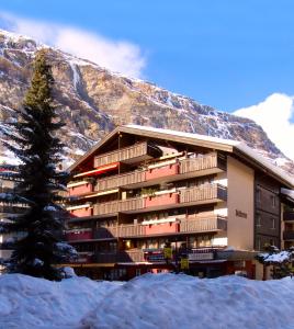 a building in the snow with a tree in front of it at Residence Bellevue in Zermatt