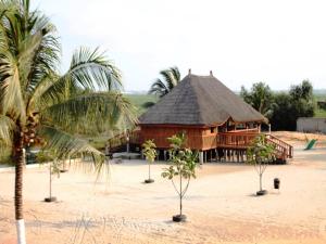 un gran edificio de madera con techo de paja y palmeras en ASSOUKA Eco-Village du lac Nokoué en Abomey-Calavi