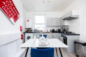 a white kitchen with a white table and blue chairs at Spacious 3 BR Near Walthamstow Station - 10 Min Walk in London