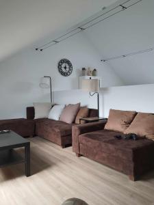 a living room with two brown couches and a clock at Gîte "Aux Pieds des Ar'den" la chambre 1 est fermée et la chambre 2 est dans le hall de nuit séparée par un rideau in Houyet