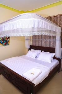 ein Schlafzimmer mit einem Himmelbett mit weißer Bettwäsche und Kissen in der Unterkunft Crown Inn Bulindo in Wakiso