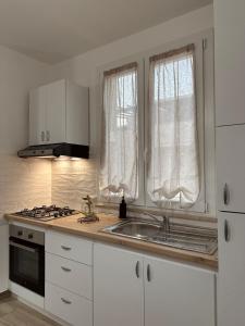 een keuken met witte kasten, een wastafel en 2 ramen bij Casa Andrew in Terrasini