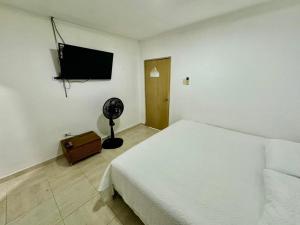 - une chambre avec un lit blanc et une télévision à écran plat dans l'établissement CASA DE HUÉSPEDES FUMINAYA, à Uribia