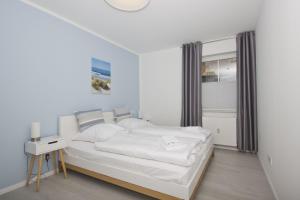 a white bedroom with a bed and a window at Haus Inselwind FeWo 09 MEERzauber - Terrasse in Groß Zicker