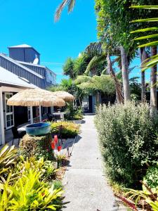 a sidewalk with a straw umbrella and chairs and plants at Southpacific Motel in Whangamata