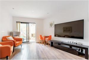 sala de estar con sillas de color naranja y TV de pantalla plana grande en Chic DuoRooms with Modern Comfort for Families, en Kent