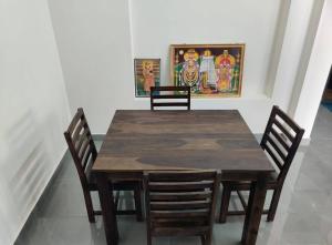 una mesa de madera con 4 sillas y un cuadro en la pared en Wind Chimes, en Tiruvannāmalai