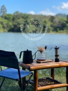 a table with a tea kettle and a chair next to a lake at Sawasdee Lagoon Camping Resort in Ban Lam Pi