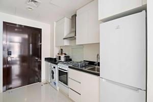 cocina con armarios blancos y nevera de acero inoxidable en Aliving Elite Studio Celestia A Dubai South en Dubái